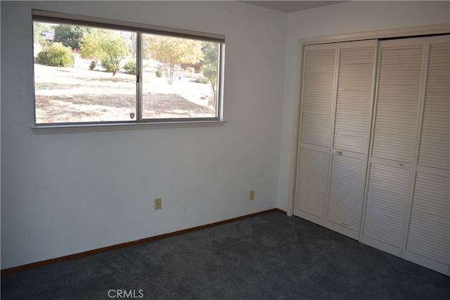 unfurnished bedroom featuring multiple windows, a closet, and dark carpet