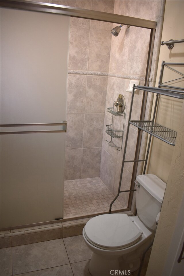 bathroom featuring toilet, tile patterned floors, and a shower with door