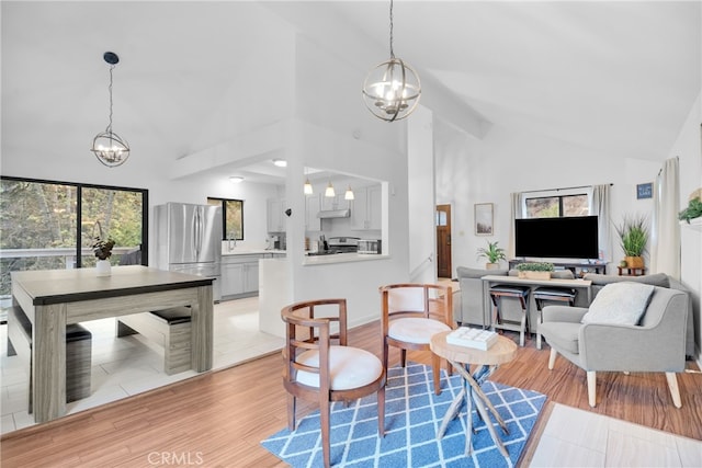 living room with light hardwood / wood-style floors, a notable chandelier, beam ceiling, and plenty of natural light