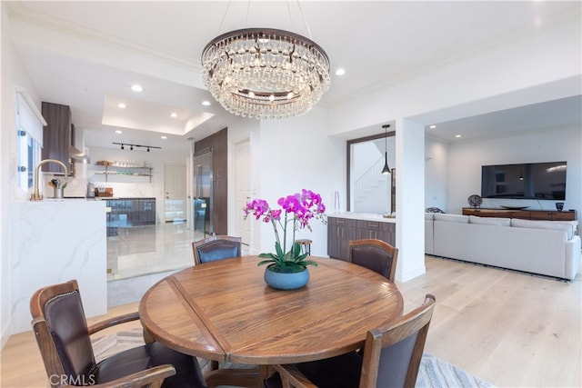 dining area with crown molding, a tray ceiling, an inviting chandelier, and light wood-type flooring