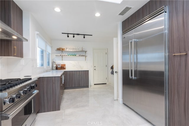 kitchen with dark brown cabinets, tasteful backsplash, wall chimney exhaust hood, and high end appliances