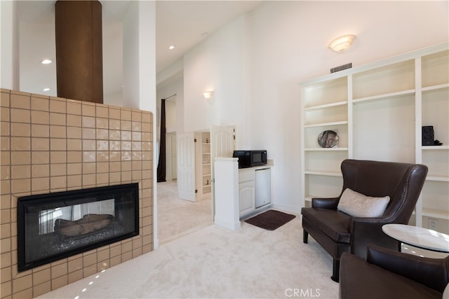 living area featuring built in features, a high ceiling, a tile fireplace, and light colored carpet