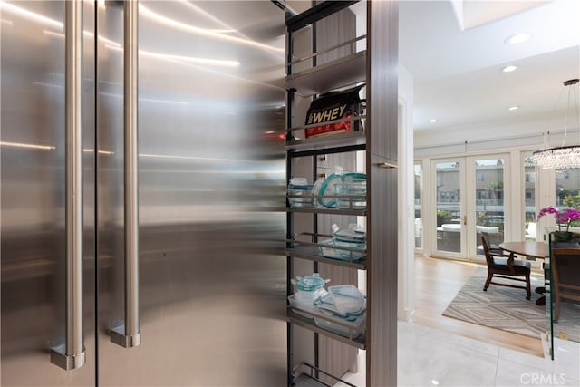 interior details featuring stainless steel fridge, crown molding, decorative light fixtures, and french doors