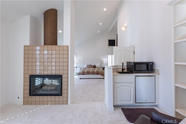 kitchen featuring sink, white dishwasher, a tiled fireplace, light carpet, and high vaulted ceiling