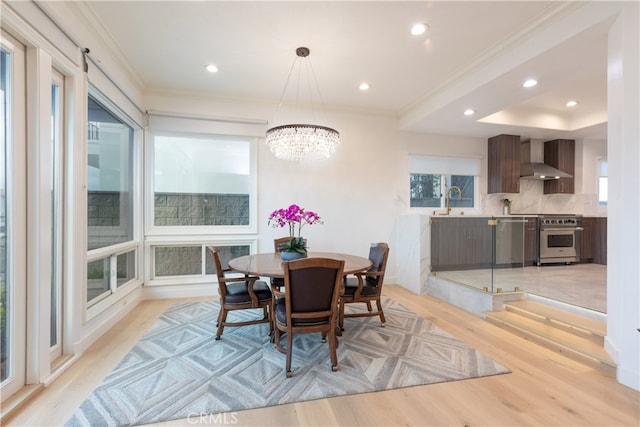 dining space with an inviting chandelier, ornamental molding, sink, and light wood-type flooring