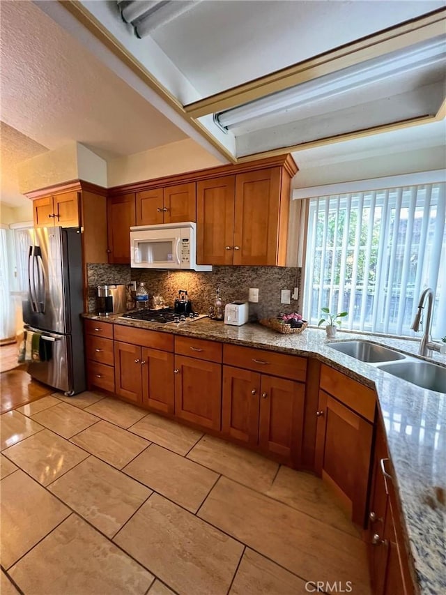 kitchen with sink, light tile patterned floors, light stone countertops, appliances with stainless steel finishes, and tasteful backsplash