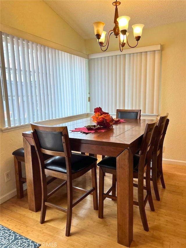 dining room featuring a textured ceiling, lofted ceiling, light hardwood / wood-style flooring, and a notable chandelier