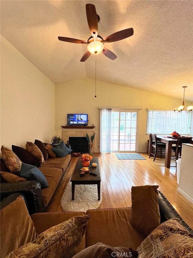 living room with ceiling fan with notable chandelier, light hardwood / wood-style floors, a textured ceiling, and vaulted ceiling