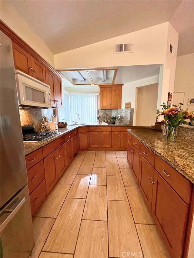 kitchen with lofted ceiling, sink, decorative backsplash, stone countertops, and stainless steel appliances