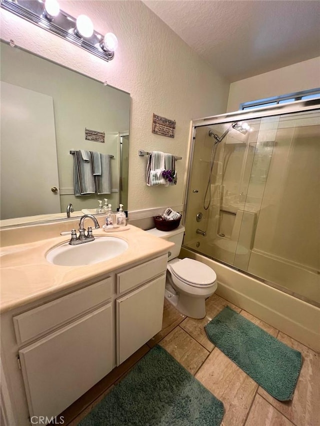 full bathroom featuring shower / bath combination with glass door, a textured ceiling, vanity, and toilet