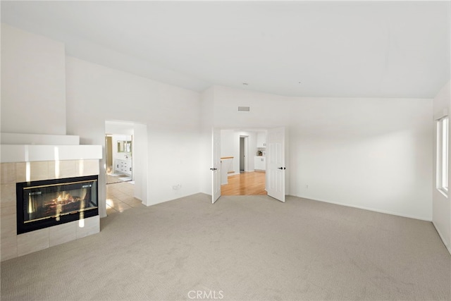 unfurnished living room featuring a fireplace, light carpet, and high vaulted ceiling