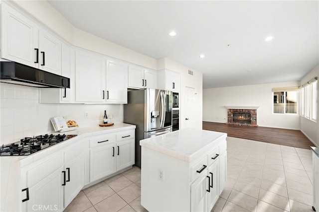 kitchen with tile countertops, white cabinets, range hood, light hardwood / wood-style floors, and gas cooktop