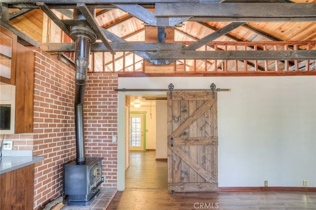 interior space with wood-type flooring, a barn door, high vaulted ceiling, and a wood stove