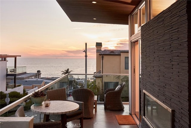 balcony at dusk featuring a water view