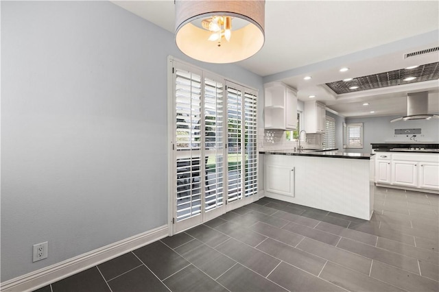 kitchen featuring white cabinets, a healthy amount of sunlight, gas stovetop, and wall chimney range hood