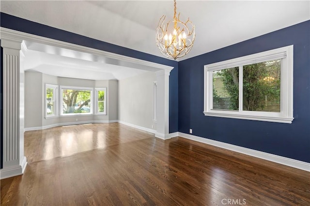 empty room with hardwood / wood-style floors, decorative columns, and an inviting chandelier