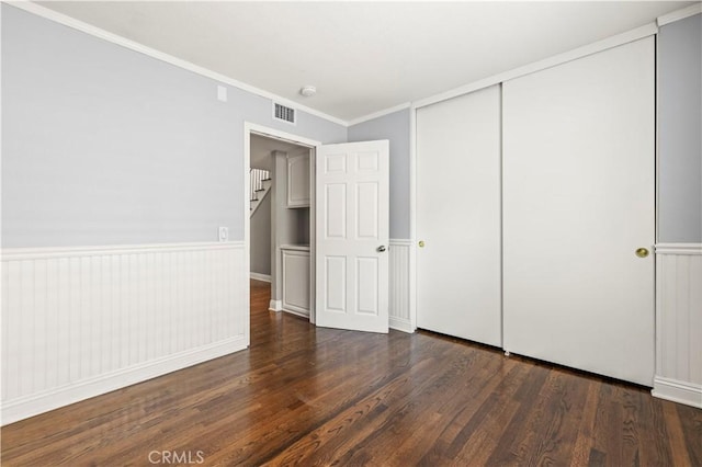 unfurnished bedroom featuring crown molding, a closet, and dark wood-type flooring