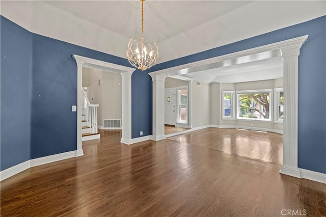 spare room with dark hardwood / wood-style flooring, an inviting chandelier, and ornate columns