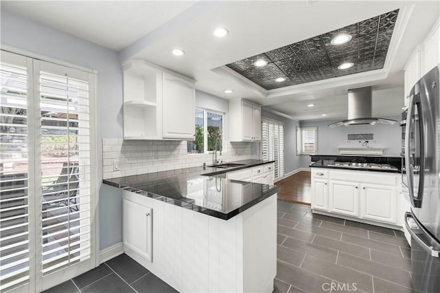 kitchen featuring kitchen peninsula, white cabinets, a healthy amount of sunlight, and wall chimney range hood