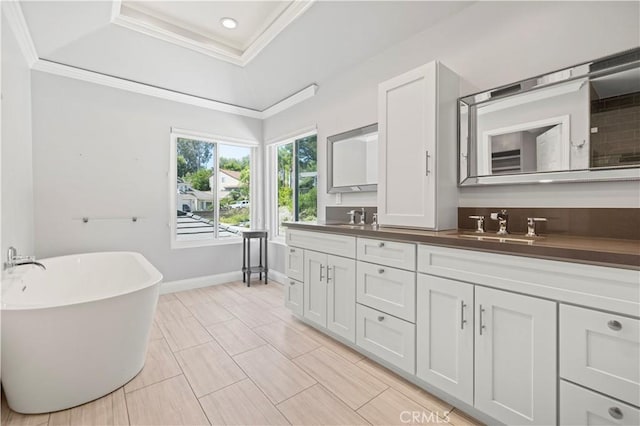 bathroom featuring a raised ceiling, vanity, a bath, and ornamental molding