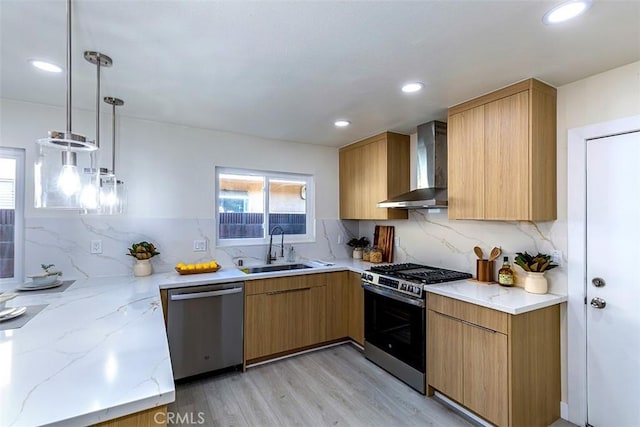 kitchen featuring pendant lighting, sink, light hardwood / wood-style flooring, wall chimney exhaust hood, and appliances with stainless steel finishes