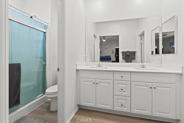 bathroom featuring hardwood / wood-style flooring, toilet, a shower with shower door, vanity, and ceiling fan