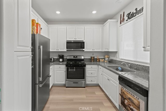 kitchen with dark stone countertops, sink, white cabinetry, appliances with stainless steel finishes, and light hardwood / wood-style floors