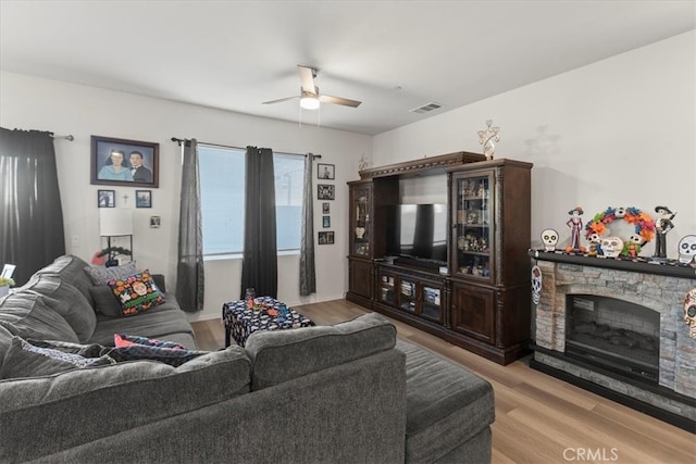 living room with a fireplace, light wood-type flooring, and ceiling fan