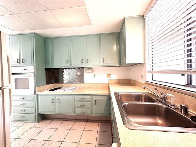 kitchen with a paneled ceiling, white appliances, sink, light tile patterned floors, and green cabinetry