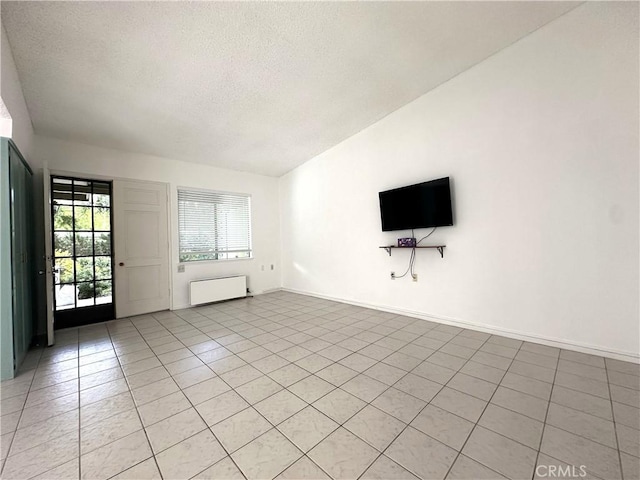 unfurnished living room with radiator heating unit, light tile patterned floors, a textured ceiling, and vaulted ceiling