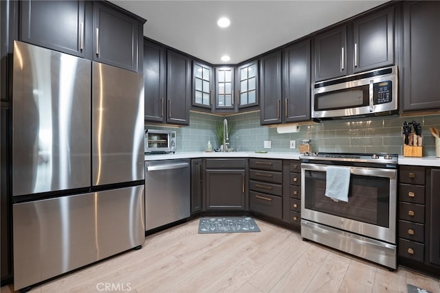 kitchen with appliances with stainless steel finishes, tasteful backsplash, sink, and light wood-type flooring