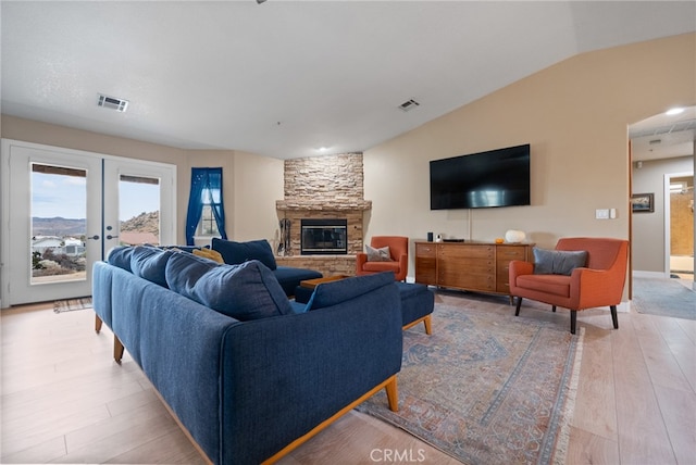 living room featuring lofted ceiling, french doors, a stone fireplace, and wood-type flooring