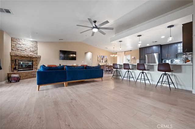 living room featuring a fireplace, ceiling fan with notable chandelier, light wood-type flooring, and vaulted ceiling