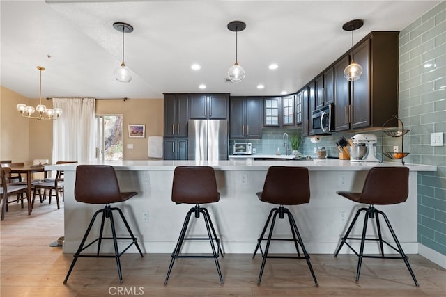 kitchen featuring light wood-type flooring, kitchen peninsula, stainless steel appliances, dark brown cabinetry, and a breakfast bar area