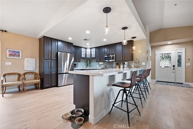 kitchen featuring appliances with stainless steel finishes, decorative light fixtures, a kitchen bar, and light hardwood / wood-style floors