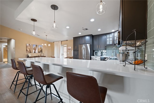 kitchen with tasteful backsplash, kitchen peninsula, hanging light fixtures, stainless steel appliances, and light hardwood / wood-style flooring