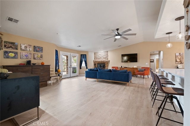 living room featuring lofted ceiling, french doors, a stone fireplace, light wood-type flooring, and ceiling fan