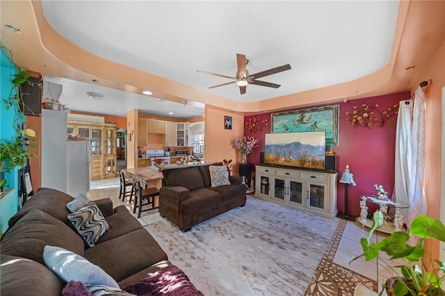 living room with a tray ceiling, ceiling fan, and light tile patterned flooring