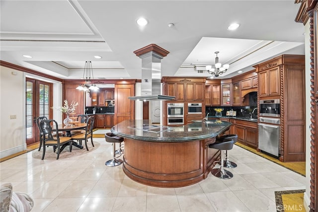 kitchen featuring hanging light fixtures, a large island, a notable chandelier, a raised ceiling, and tasteful backsplash