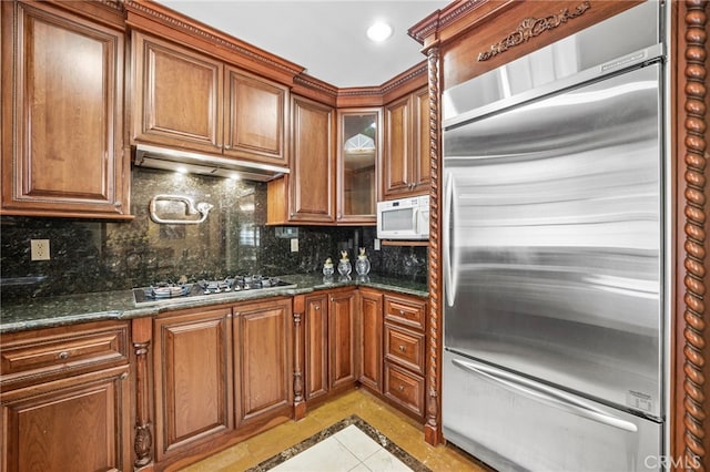 kitchen with dark stone countertops, stainless steel appliances, decorative backsplash, and light tile patterned flooring