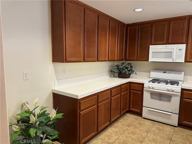 kitchen with tile countertops, light tile patterned floors, and white appliances