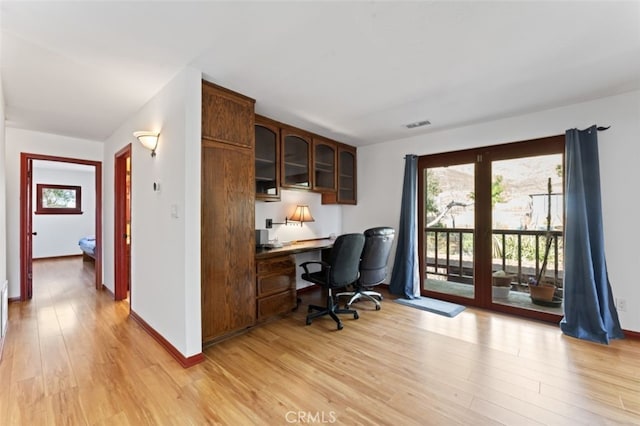 office space with built in desk and light hardwood / wood-style flooring