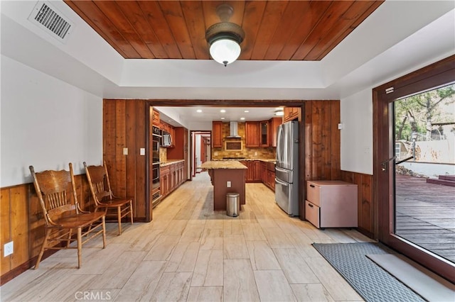 kitchen with appliances with stainless steel finishes, a center island, wooden walls, and tasteful backsplash