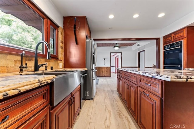 kitchen with sink, light stone counters, backsplash, double oven, and stainless steel fridge