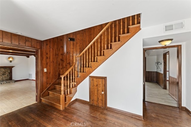 stairs with hardwood / wood-style floors, a stone fireplace, and wooden walls