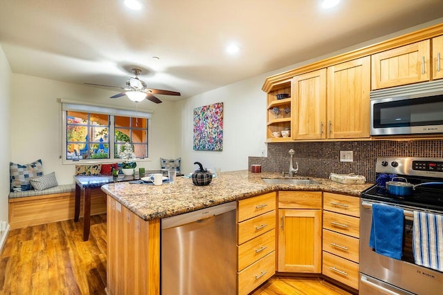 kitchen featuring kitchen peninsula, light stone countertops, stainless steel appliances, sink, and light hardwood / wood-style flooring