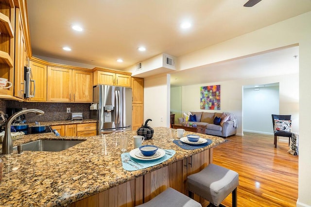 kitchen with sink, light hardwood / wood-style flooring, dark stone countertops, appliances with stainless steel finishes, and tasteful backsplash