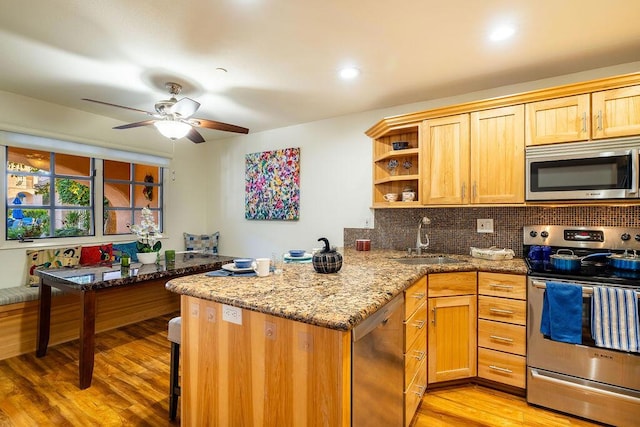 kitchen with sink, light stone counters, backsplash, appliances with stainless steel finishes, and light wood-type flooring