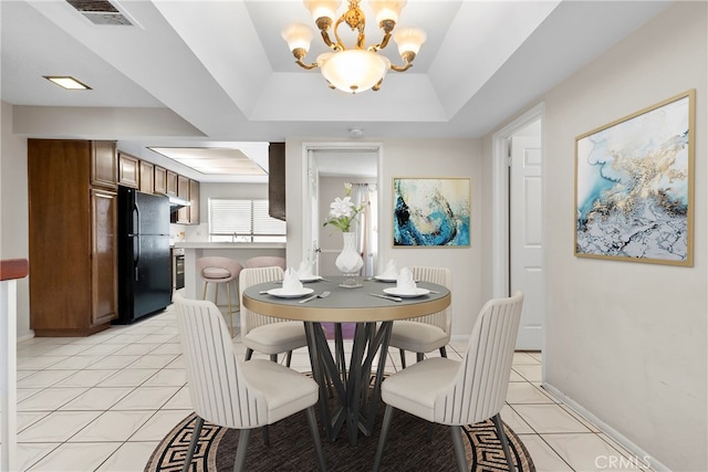 dining room featuring an inviting chandelier, light tile patterned flooring, and a tray ceiling