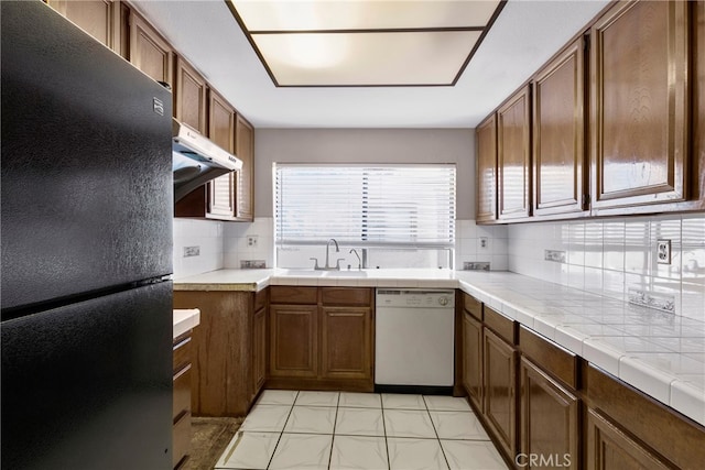 kitchen with tasteful backsplash, sink, dishwasher, tile counters, and black refrigerator